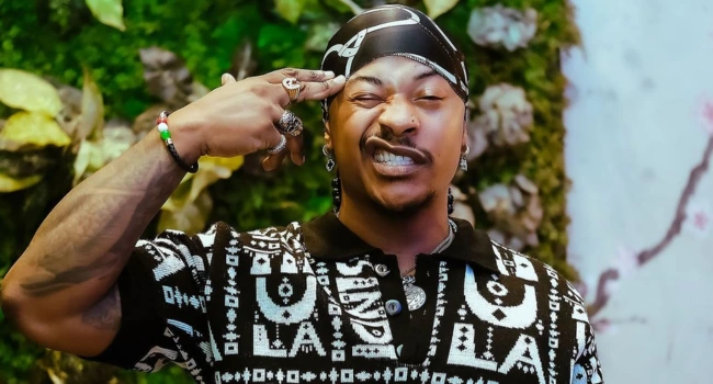 Priddy Ugly posing outdoors in a patterned shirt and bandana