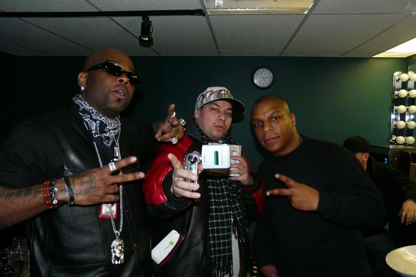 Three men posing indoors, one at right making a hand gesture